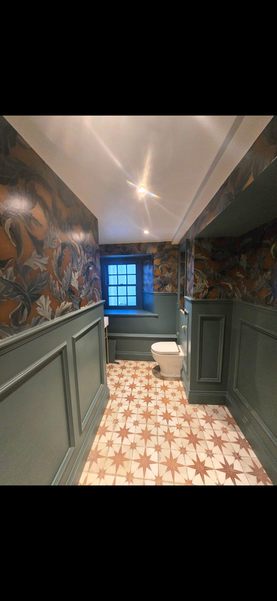 Deep sage green wall paneling and decorative botanical wallpaper in a luxury bathroom