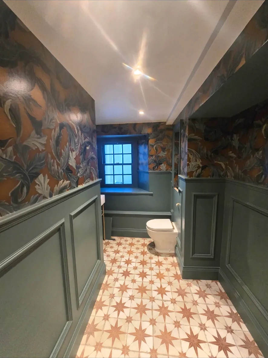 Deep sage green wall paneling and botanical wallpaper in a luxury bathroom in Market Harborough