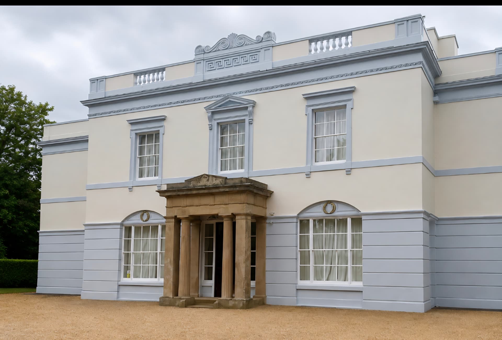 Grand period house exterior painted in pale cream with grey-blue joinery and a stone-columned entrance porch — Leicestershire