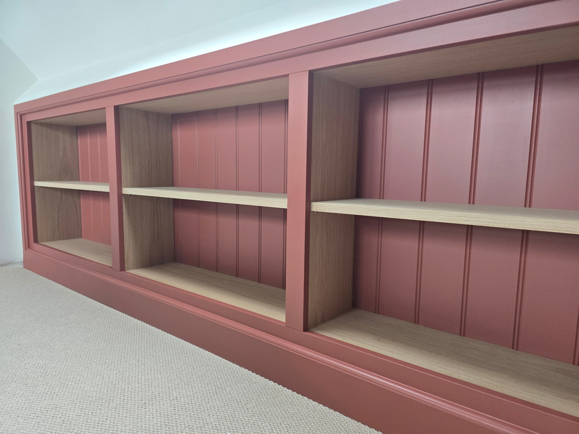 Bespoke alcove shelving unit hand-sprayed in a deep rusted red with oak shelving and tongue-and-groove backing
